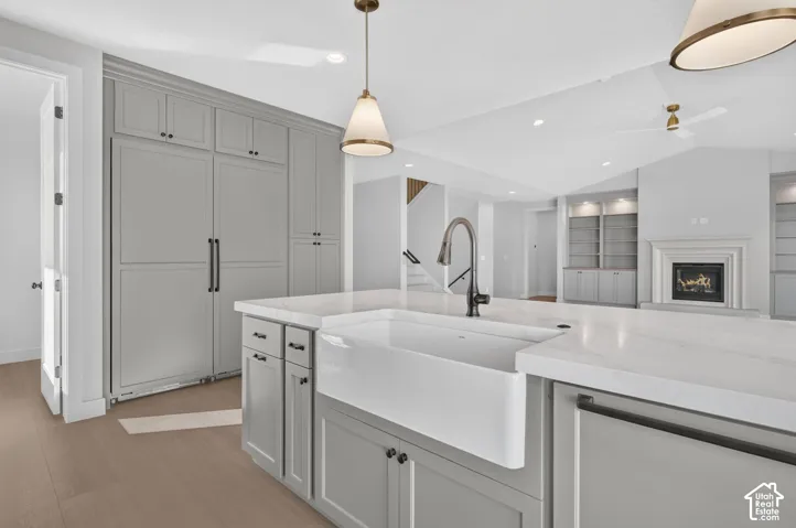 Kitchen featuring a central island with a white apron-front sink, stone-finish countertops, panel-ready cabinetry, and pendant lighting