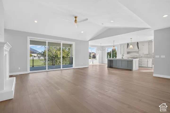 Open-concept area featuring vaulted ceilings, wood-finish flooring, a white mantle fireplace, recessed lighting, and a kitchen with a central island and shaker-style cabinetry