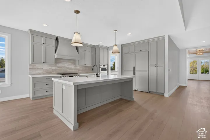 Kitchen featuring grey shaker-style cabinetry, a center island with quartz countertops, wood-finish flooring, a tile backsplash, and stainless steel integrated appliances