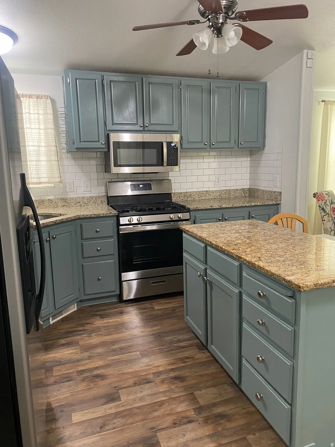 Kitchen featuring teal cabinetry, stone-finish countertops, subway tile backsplash, stainless steel appliances, and wood-finish flooring