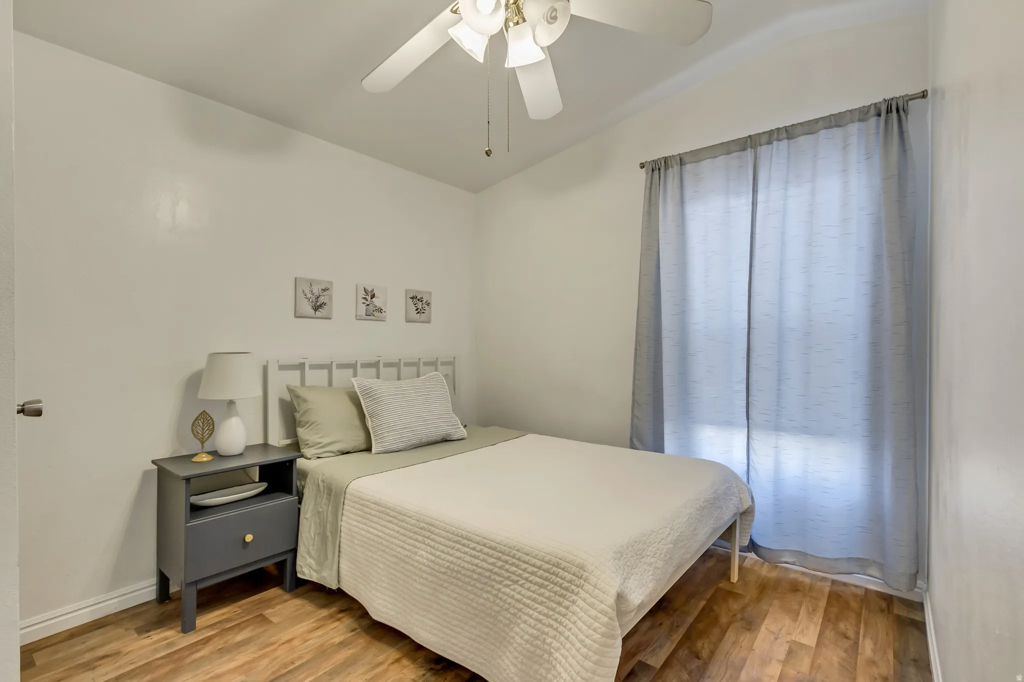 Wood-finish flooring, ceiling fan, window with curtain rod, and white walls