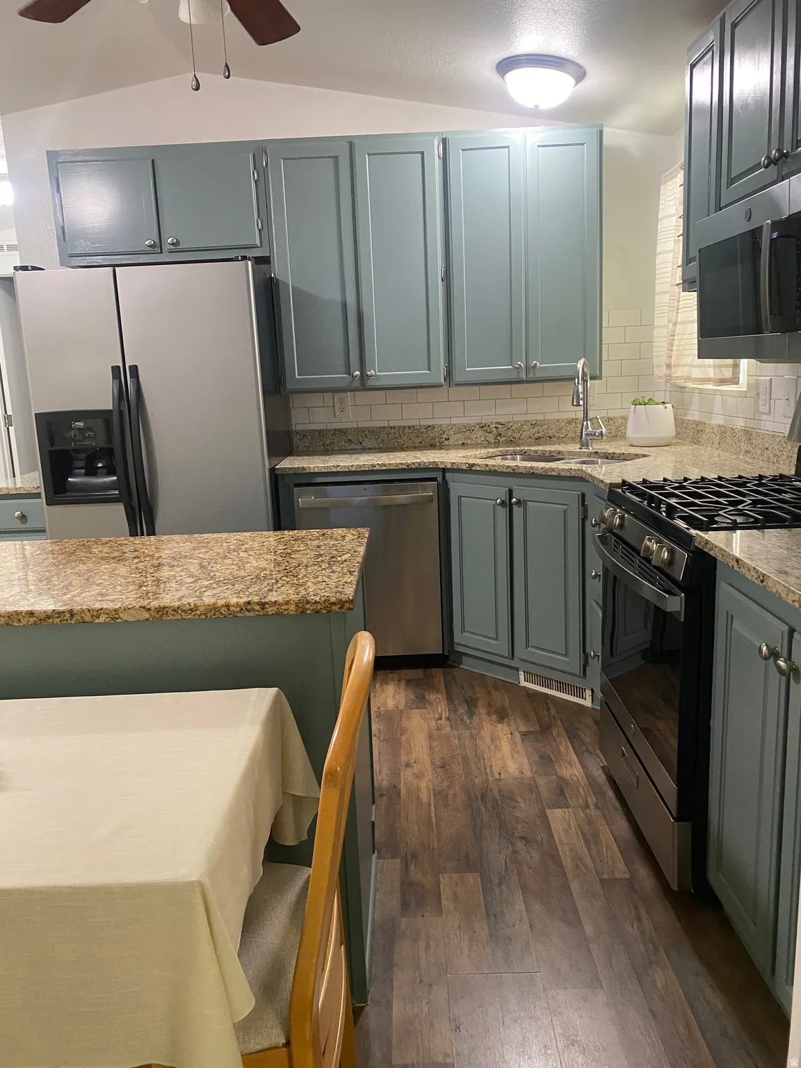 Kitchen featuring wood-finish flooring, light-toned cabinetry, stainless steel appliances, a white subway tile backsplash, and stone countertops