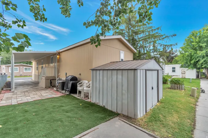 Exterior featuring covered parking, a metal storage shed, a paved patio, and a grass area