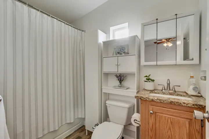 Wood-finish flooring, white vanity with a granite-style countertop, undermount sink, and a mirrored medicine cabinet