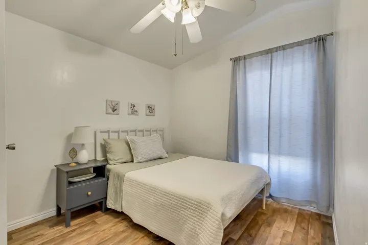 Wood-finish flooring, ceiling fan, window with curtain rod, and white walls