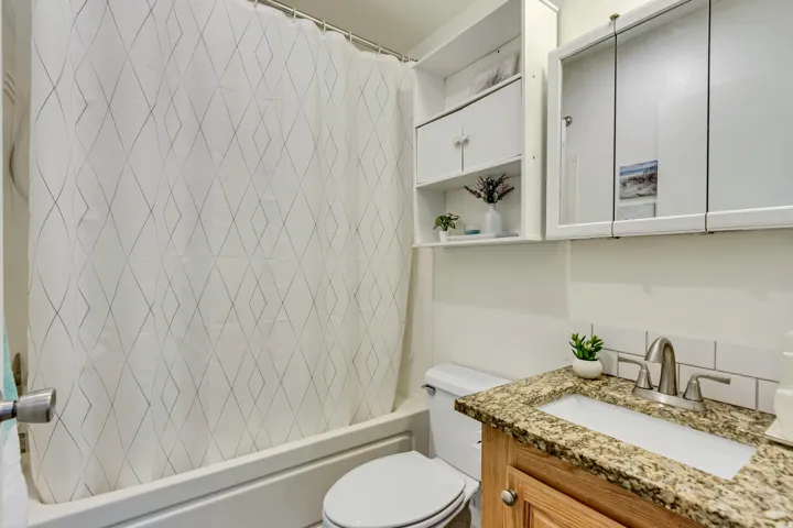 White subway tile backsplash, wood-finish vanity with granite-style countertop, undermount sink, and brushed nickel fixtures