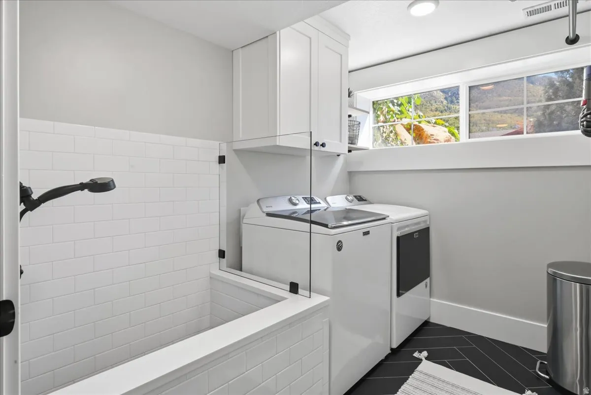 Built-in tiled utility tub with shower sprayer, white shaker-style cabinetry, and dark herringbone-patterned flooring