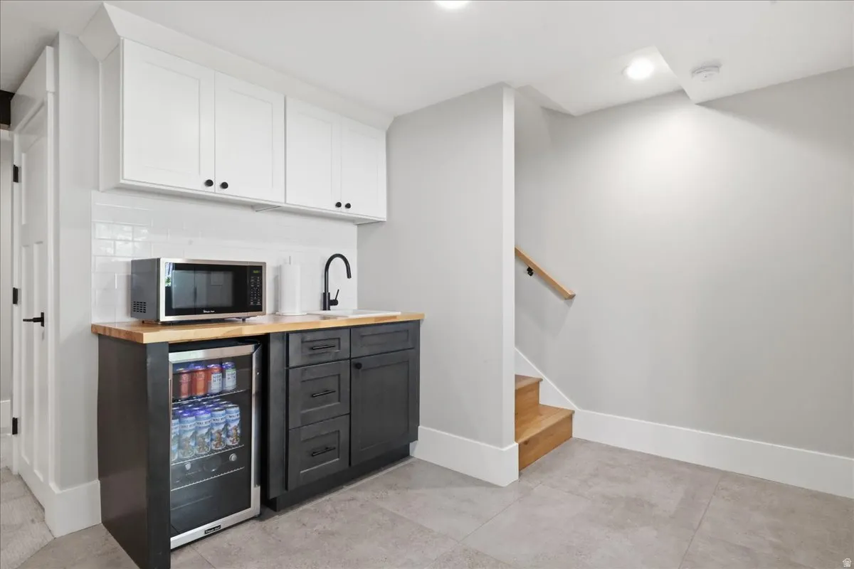 Wet bar featuring white upper cabinetry, dark lower cabinetry, a wood-finish countertop, a stainless steel beverage refrigerator, and a matte black faucet