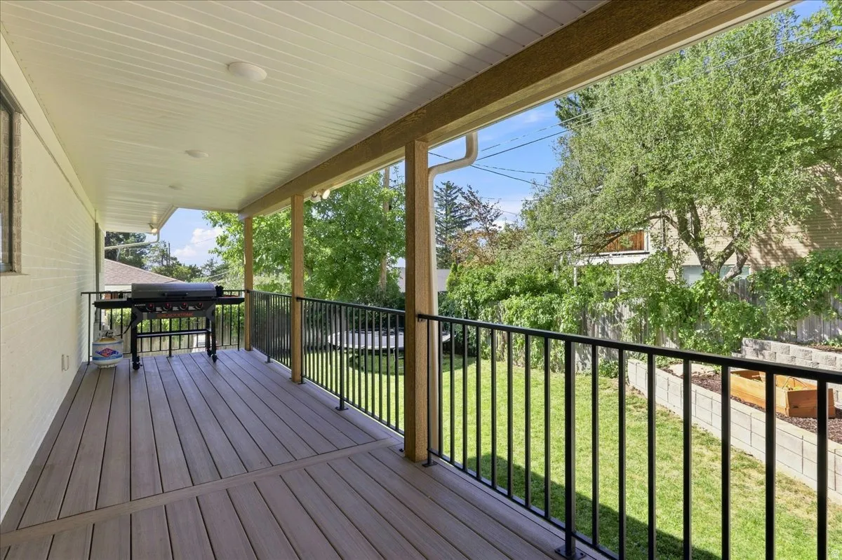 Covered patio featuring composite decking, white brick exterior, black metal railing, and recessed lighting