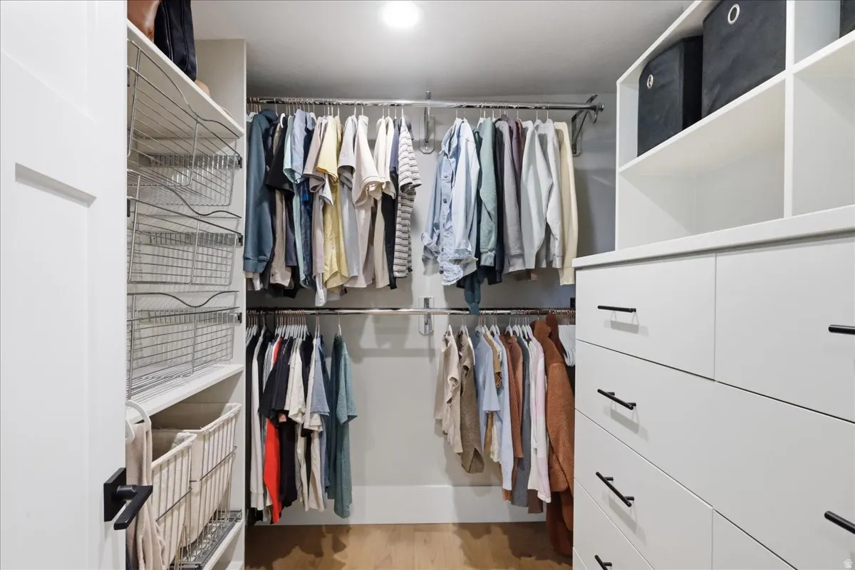 Built-in closet system featuring multiple hanging rods, white cabinetry with black hardware, open shelving, and wood-finish flooring