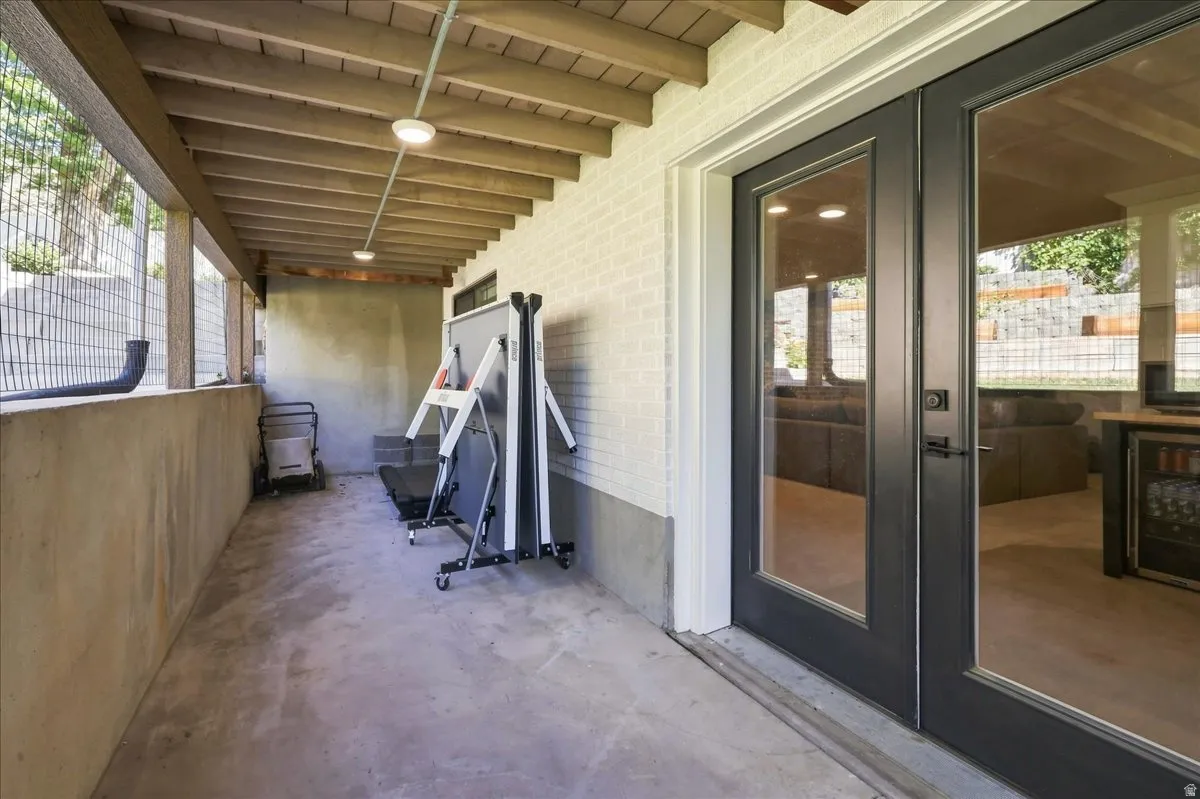 Covered patio with a concrete floor, exposed wood beam ceiling, and white painted brick wall