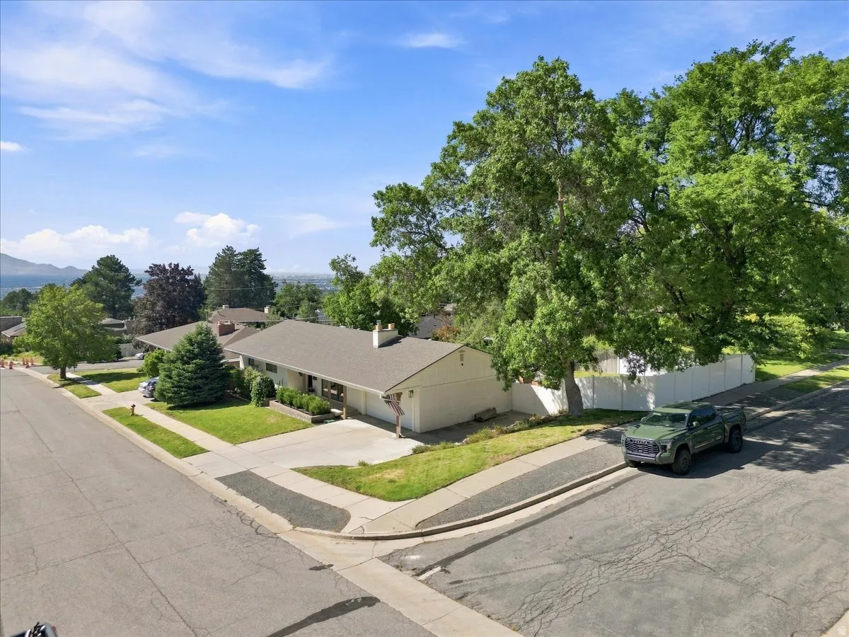 Ranch-style residence featuring a prominent front lawn, an attached garage, and mature trees