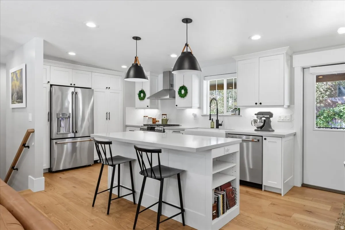 White shaker cabinetry, stainless steel appliances, central island with seating, wood-finish flooring, recessed and pendant lighting