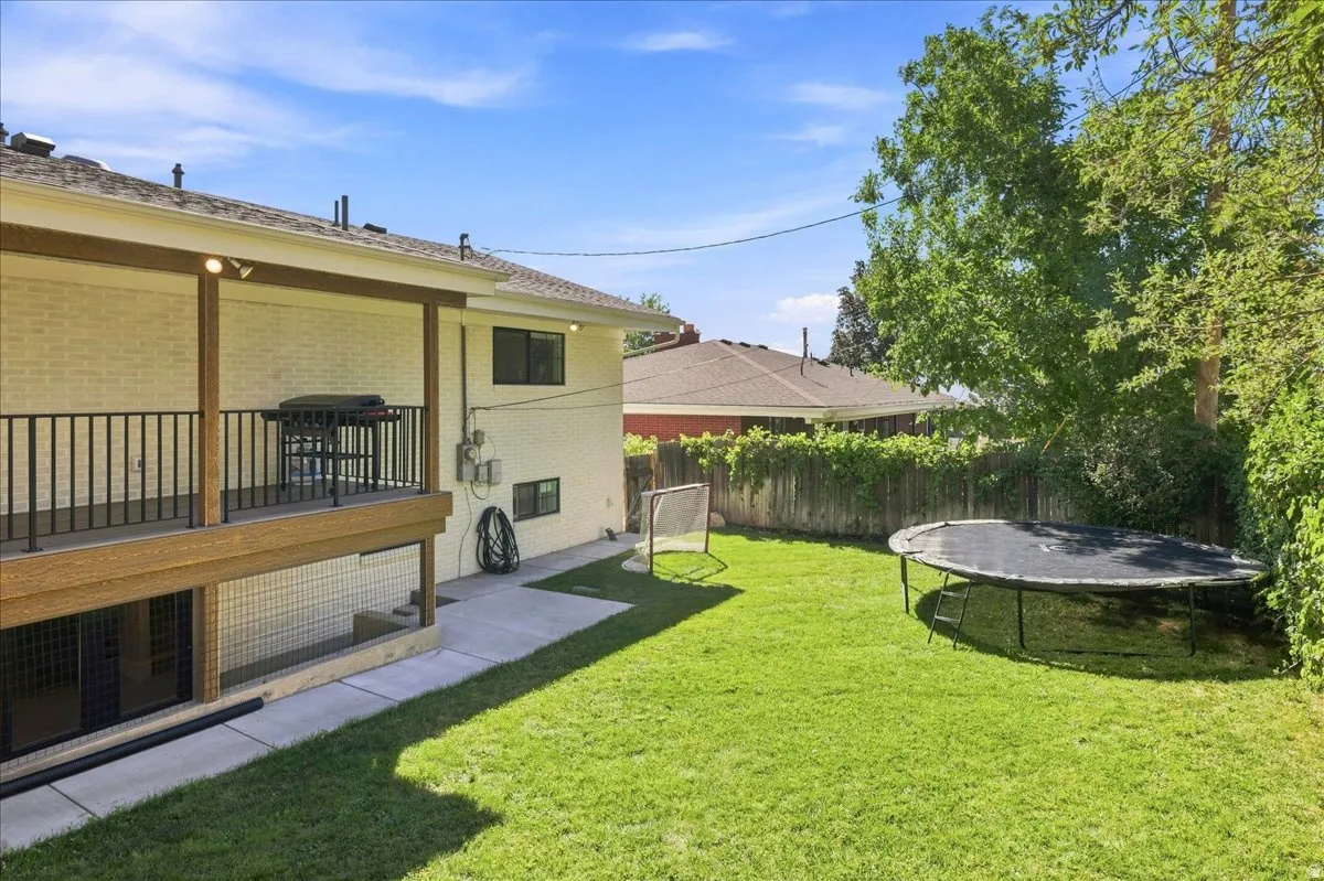 Expansive green lawn with mature perimeter trees, a covered patio with recessed lighting, and a concrete pathway