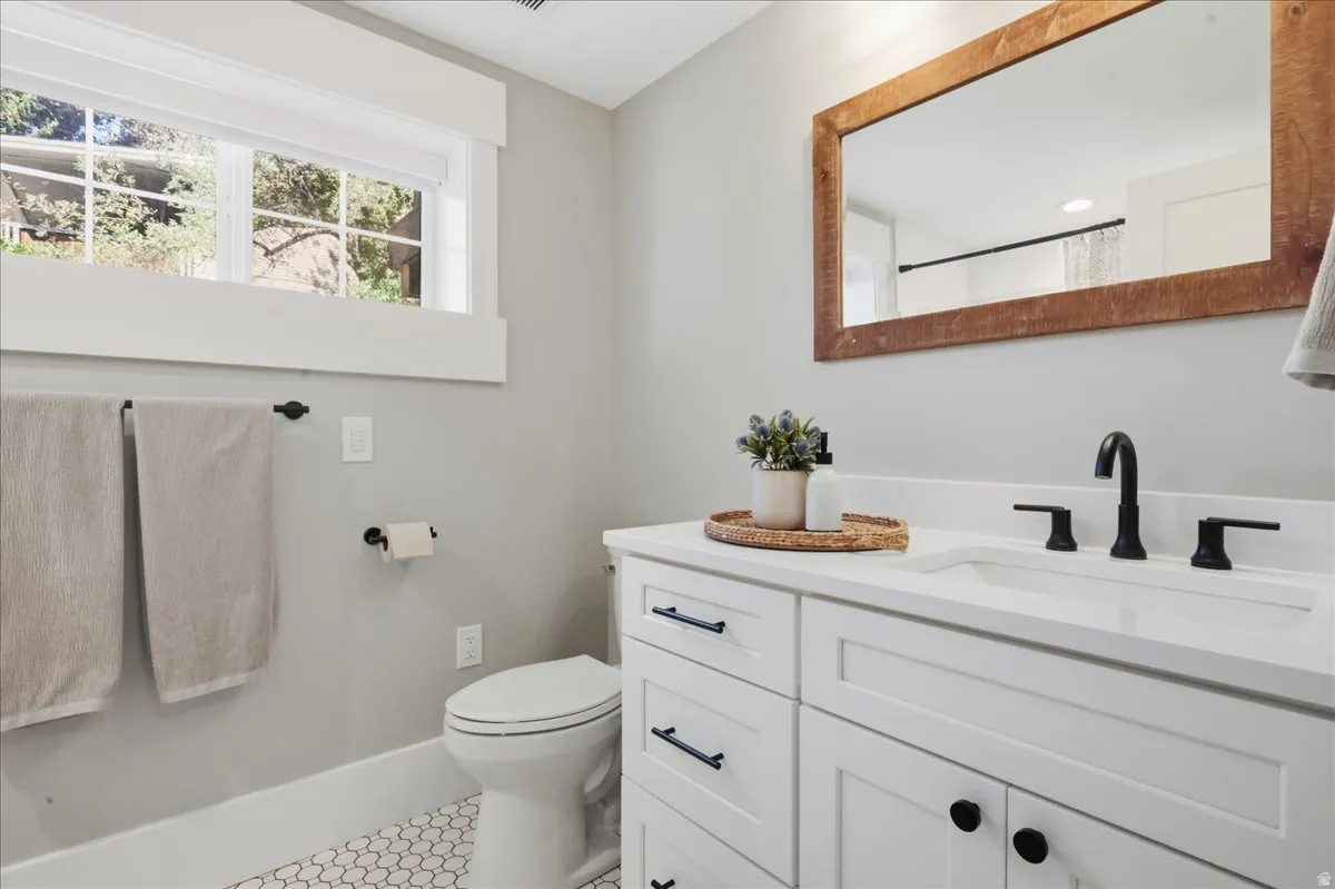 White vanity with a solid surface countertop, matte black fixtures, honeycomb floor tile, and a rectangular mirror with a wood frame