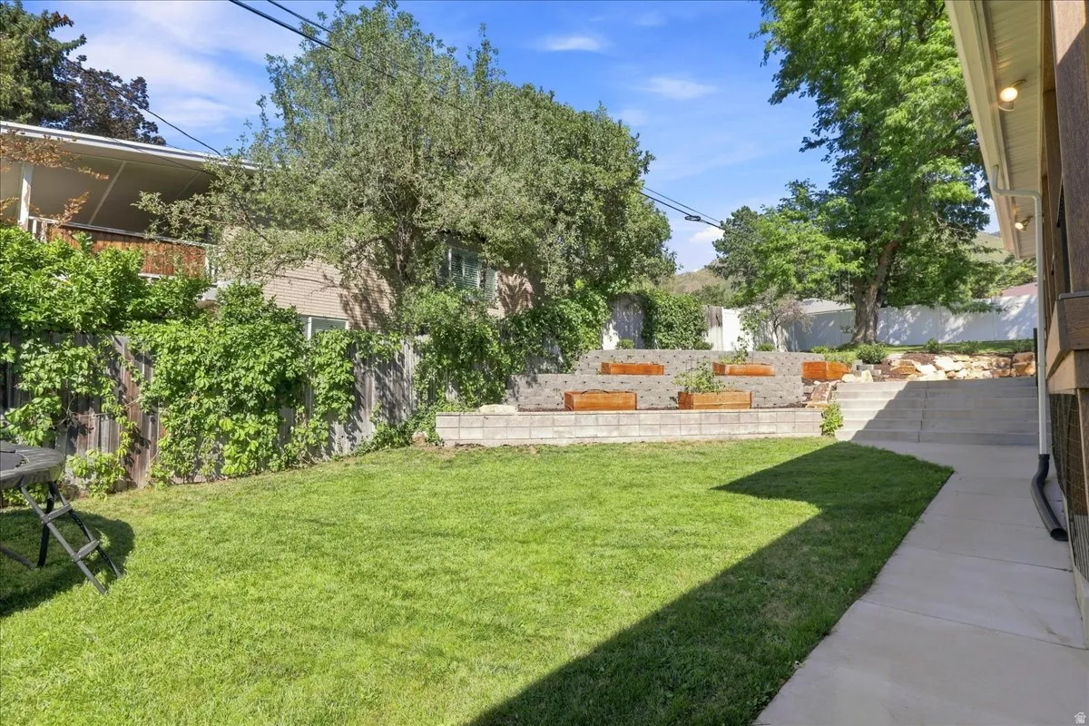 Expansive lawn area with a concrete pathway, tiered retaining walls, and integrated planters