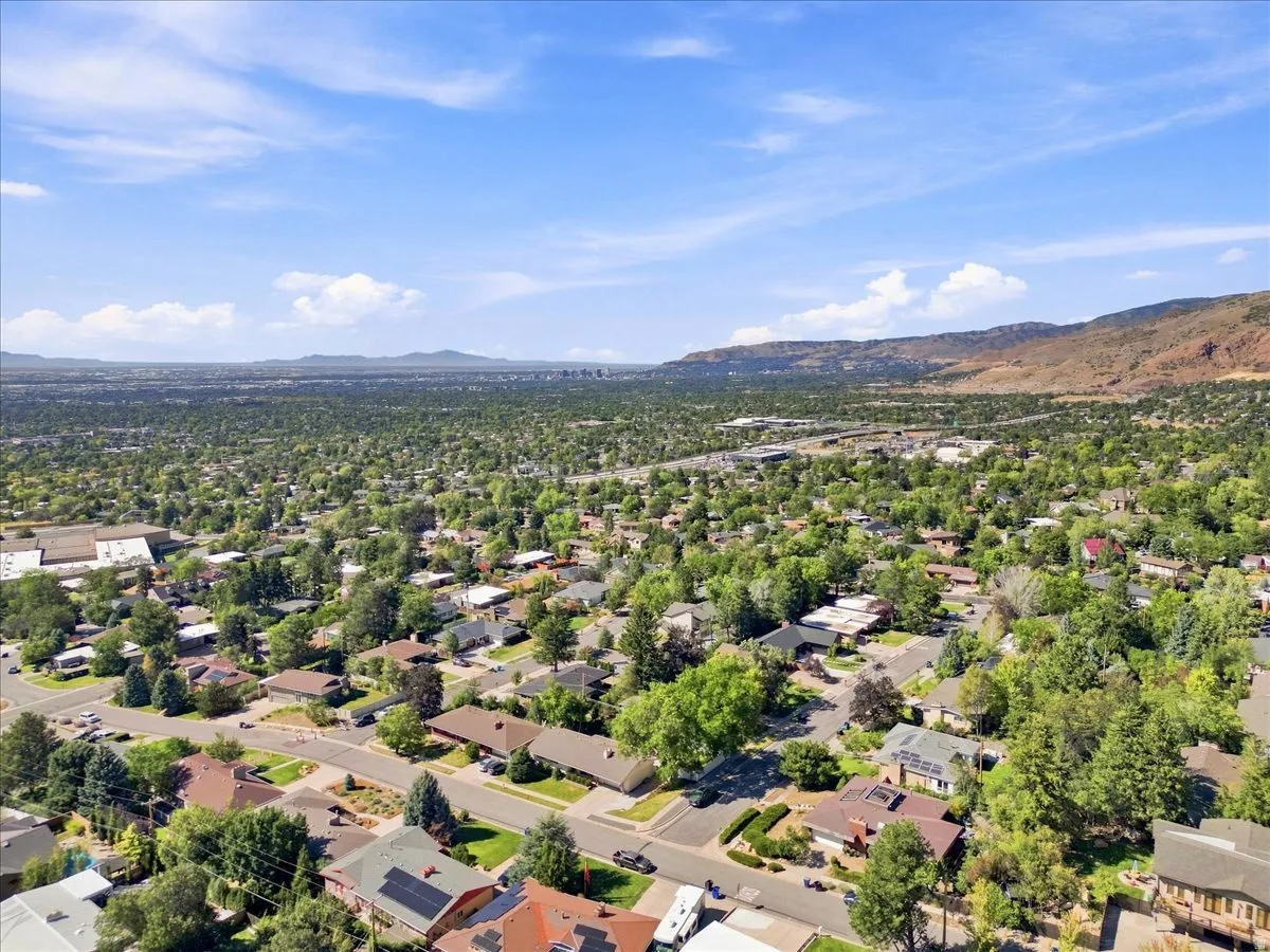 Residential neighborhood featuring a mix of mature trees and established homes, with distant mountains and a large urban expanse visible under a clear sky