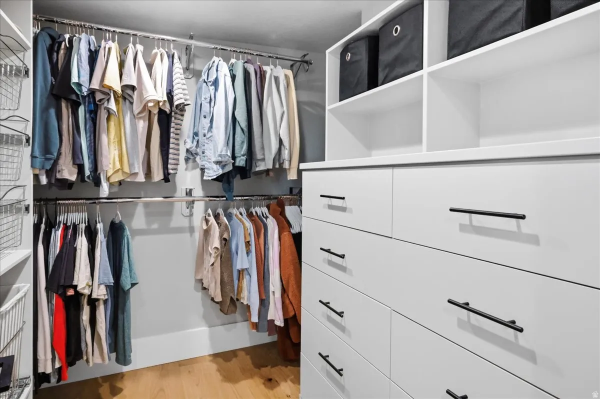 Integrated closet system featuring white cabinetry, multiple drawers with dark hardware, open shelving, and dual hanging rods