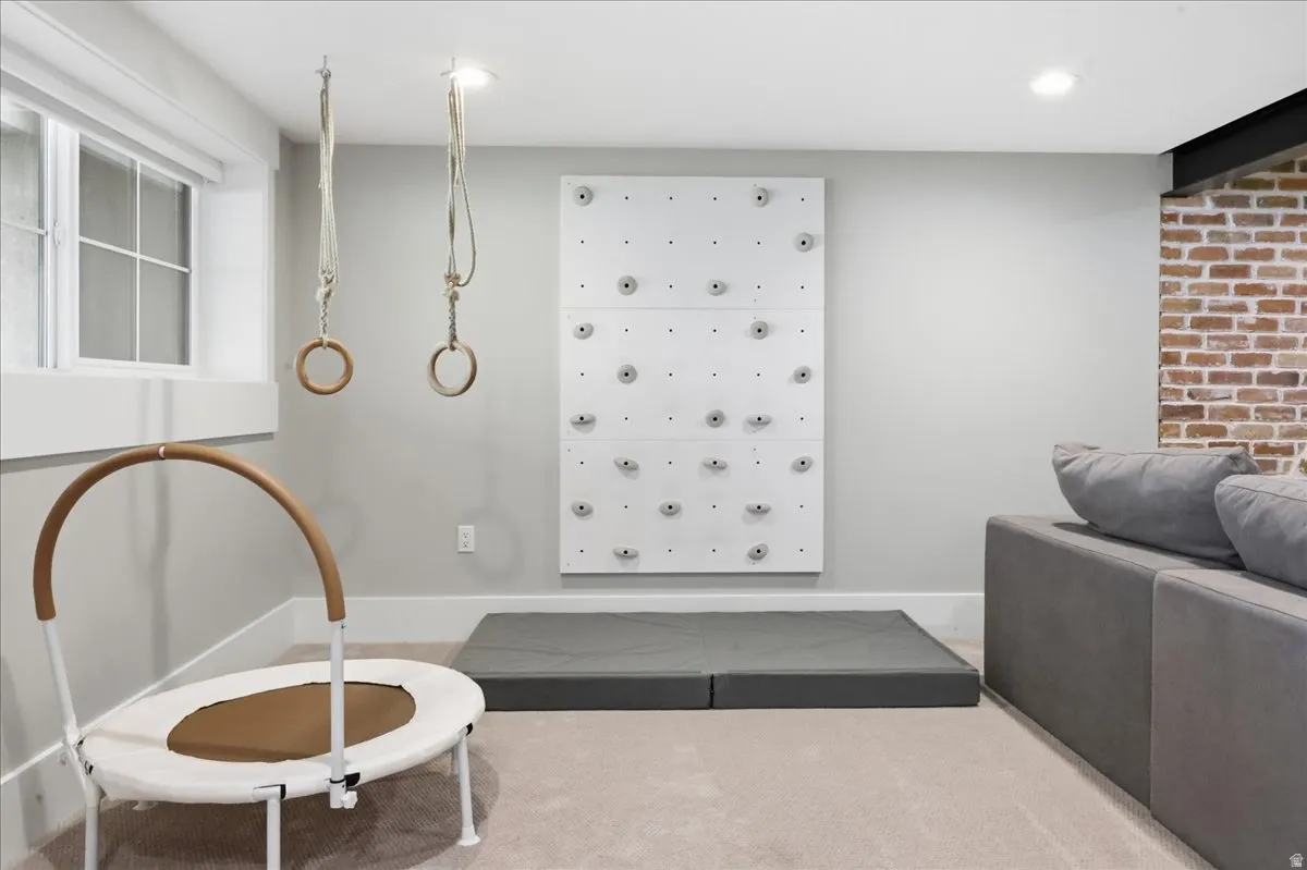 Recessed lighting illuminates a built-in climbing wall, exposed brick accent, window with grid panes, and permanent ceiling-mounted gymnastic rings