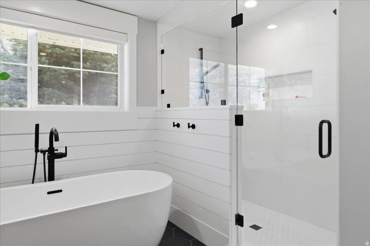 Freestanding tub with a matte black floor-mounted faucet, glass-enclosed shower with matte black hardware, white subway tile shower surround, shower niche, and hexagonal floor tiles