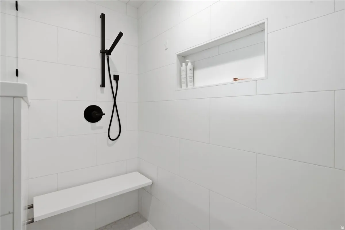 Shower featuring large format white tile, a matte black shower system, a built-in shower niche, and an integrated shower bench