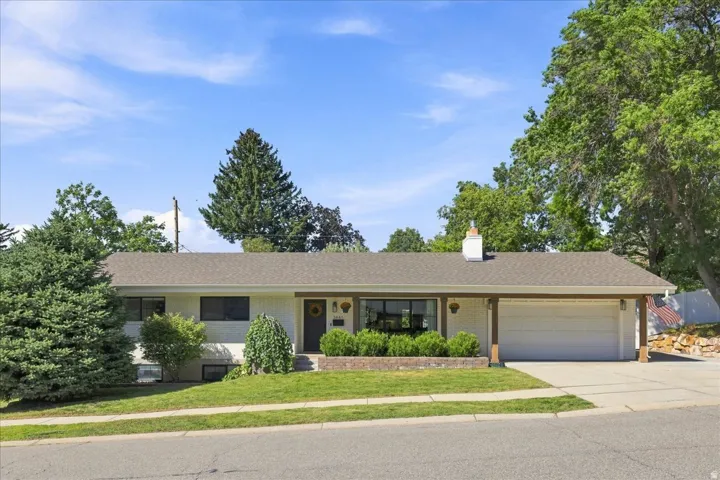 Ranch-style residence featuring a prominent front lawn, an attached two-car garage, and mature landscaping