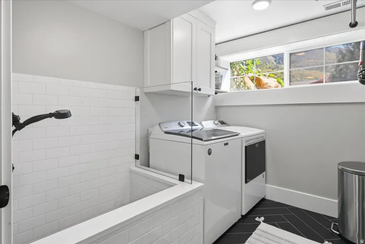 Built-in tiled utility tub with shower sprayer, white shaker-style cabinetry, and dark herringbone-patterned flooring