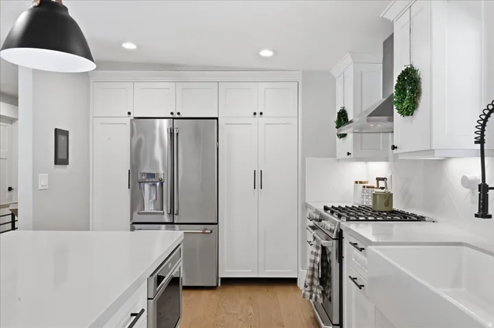 White shaker cabinetry, stainless steel appliances, herringbone tile backsplash, recessed lighting, and a farmhouse sink