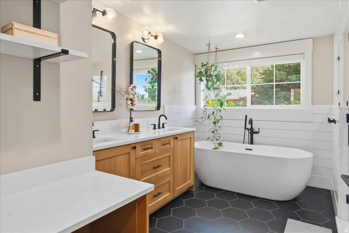 Dual vanity with light wood finish cabinetry, white countertops, and matte black fixtures