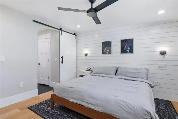 Wood-finish flooring, white shiplap accent wall, modern ceiling fan, recessed lighting, and a white barn door