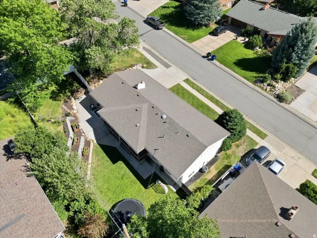 Asphalt shingle roof, paved driveway, mature trees, landscaped backyard, and a manicured lawn