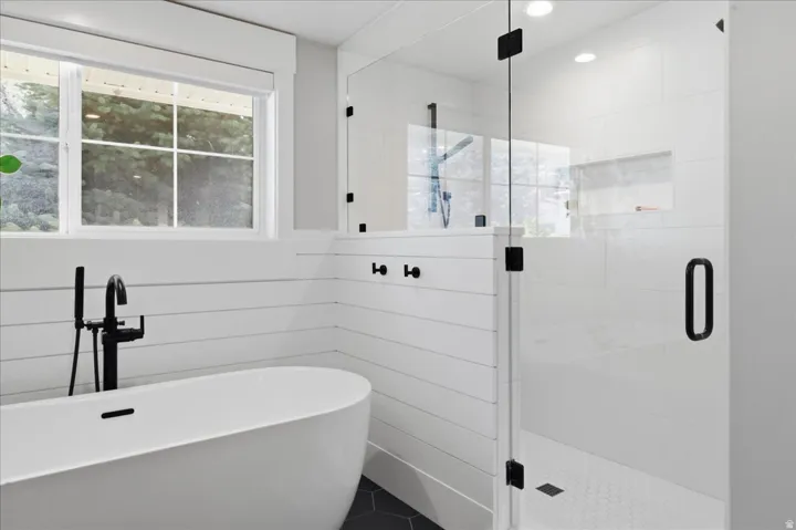 Freestanding tub with a matte black floor-mounted faucet, glass-enclosed shower with matte black hardware, white subway tile shower surround, shower niche, and hexagonal floor tiles