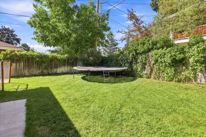 Expansive backyard featuring a manicured lawn, mature trees, and privacy fencing with established greenery