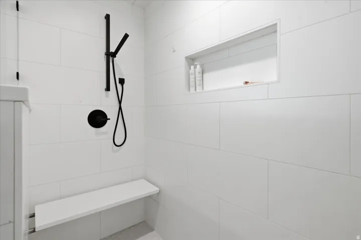 Shower featuring large format white tile, a matte black shower system, a built-in shower niche, and an integrated shower bench