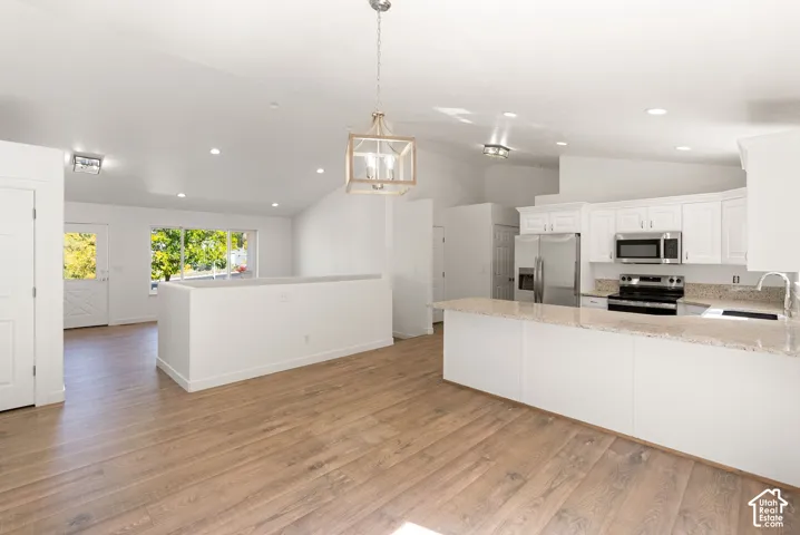 Vaulted ceilings with recessed lighting, wood-finish flooring, white kitchen cabinetry, light-toned countertops, and stainless steel kitchen appliances