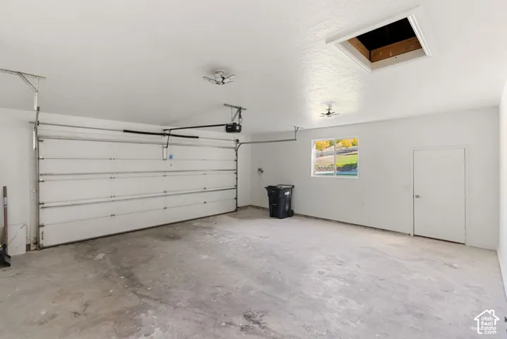 Attached garage with a white sectional door, concrete flooring, and a single window
