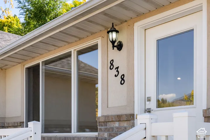 White entry door with a full-length glass insert, exterior wall sconce, and black numerical address