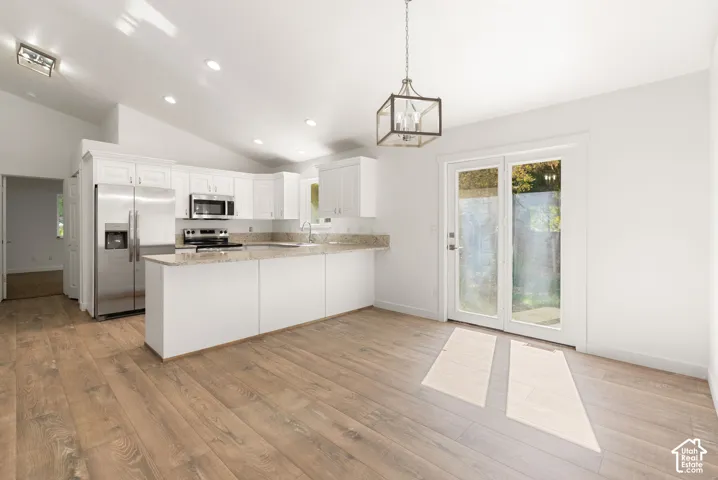 Vaulted ceiling, recessed lighting, wood-finish flooring, white cabinetry with stainless steel appliances, and double glass panel doors