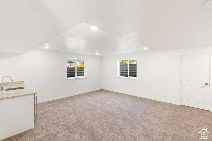 Recessed lighting, carpeted flooring, two windows, and a built-in wet bar with a granite countertop and stainless steel faucet