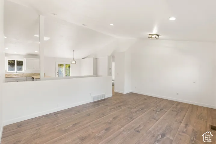 Vaulted ceilings, wood-finish flooring, recessed lighting, and a contemporary ceiling fixture