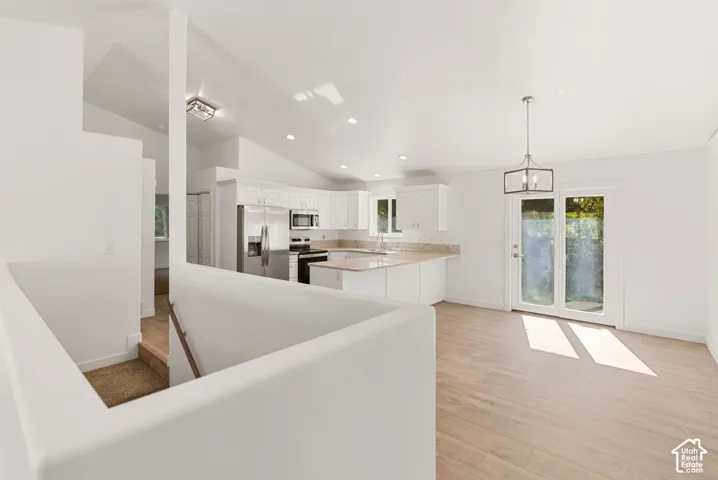 Vaulted ceilings, white shaker cabinetry, stainless steel appliances, light wood-finish flooring, and French doors