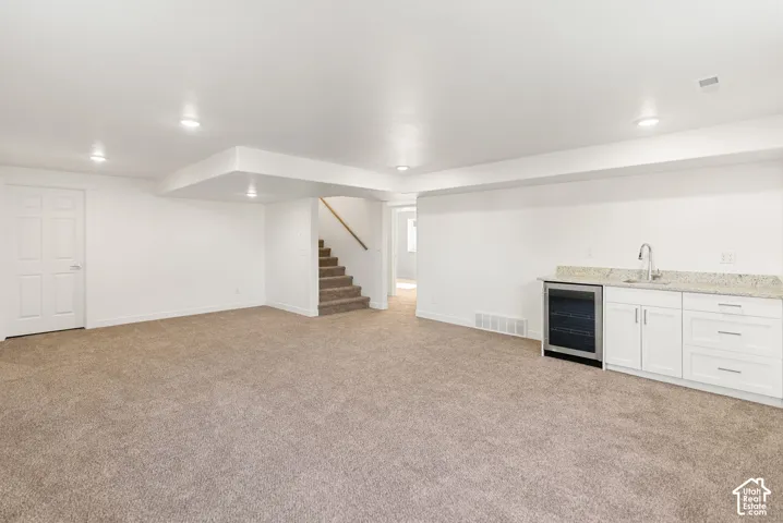 Recessed lighting, light brown carpet, white cabinetry, granite-style countertop, and stainless steel beverage cooler