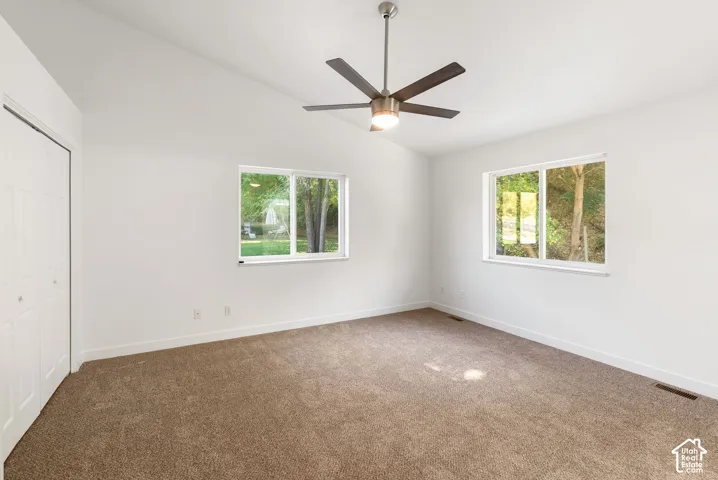 Vaulted ceiling with a ceiling fan, two windows, carpet flooring, and bi-fold closet doors