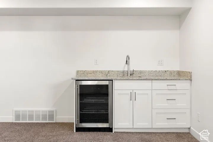 Built-in beverage cooler, white cabinetry, undermount sink with a gooseneck faucet, light-toned countertop, and white walls