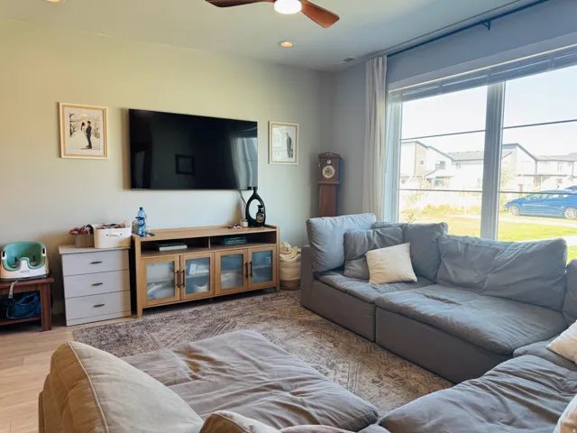 Recessed ceiling lighting, a ceiling fan, light wood-finish flooring, and a large window with roller shades
