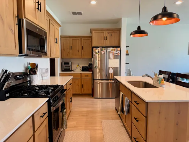 Kitchen featuring wood-finish cabinetry, stainless steel appliances, white countertops, and wood-finish flooring