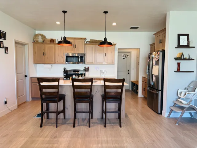 Open-concept kitchen featuring light wood cabinetry, a center island with seating, stainless steel appliances, and wood-finish flooring