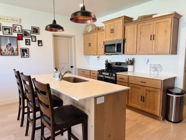 Spacious kitchen featuring an expansive center island with an undermount sink, light wood-finish cabinetry, stainless steel appliances, and two pendant light fixtures