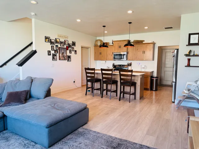 Open-concept living space featuring wood-finish flooring, a kitchen island with seating, pendant lighting, stainless steel appliances, and wood cabinetry