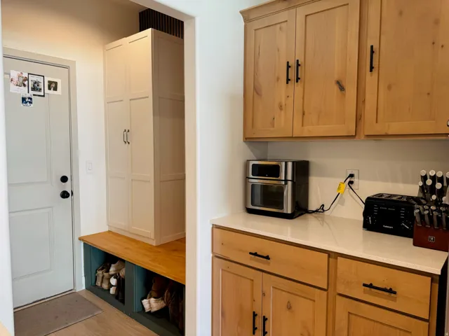Wood-finish flooring, built-in storage bench, and tall built-in cabinetry complement the light wood-finish kitchen cabinetry and light-toned countertop